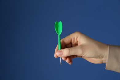 Photo of Woman holding dart on blue background, closeup. Space for text