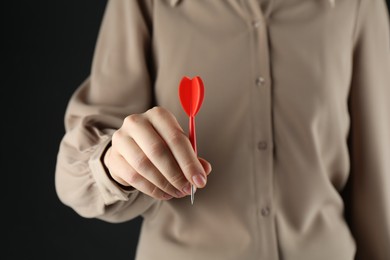 Photo of Woman holding dart on black background, closeup