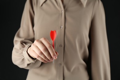 Photo of Woman holding dart on black background, closeup