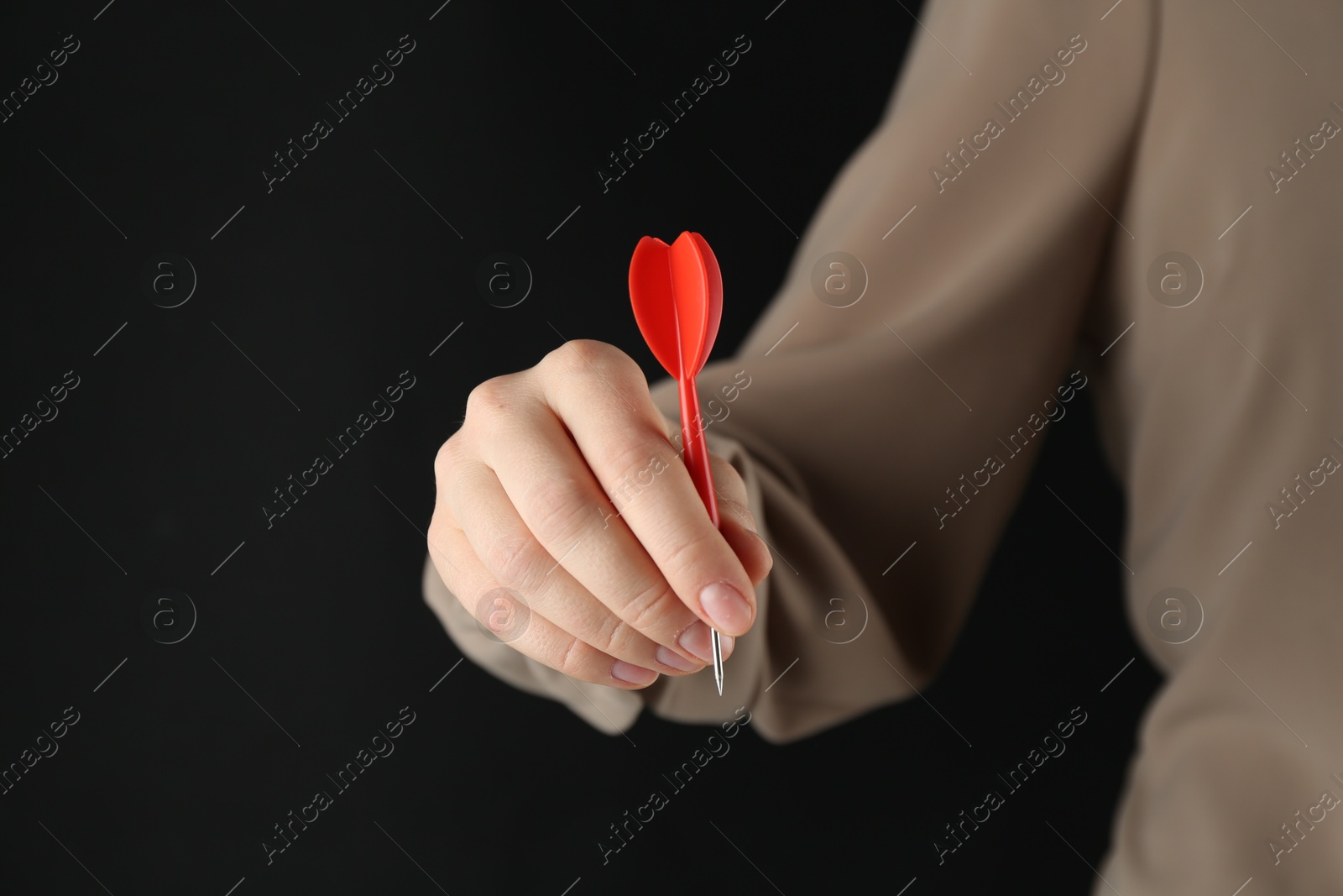 Photo of Woman holding dart on black background, closeup