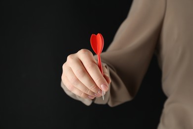 Photo of Woman holding dart on black background, closeup