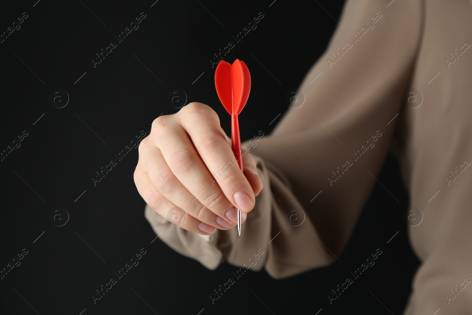 Photo of Woman holding dart on black background, closeup