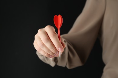 Photo of Woman holding dart on black background, closeup