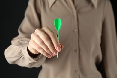 Photo of Woman holding dart on black background, closeup