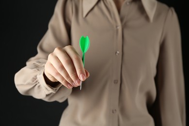 Photo of Woman holding dart on black background, closeup