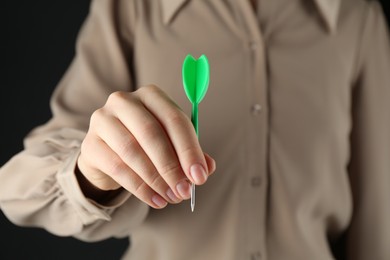 Photo of Woman holding dart on black background, closeup