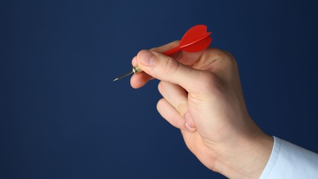 Photo of Man holding dart on blue background, closeup. Space for text