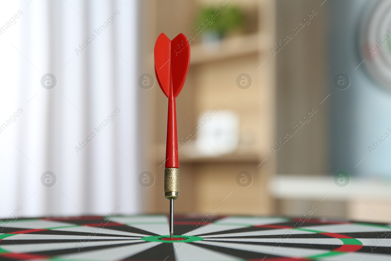 Photo of Red arrow hitting target on dart board indoors, closeup