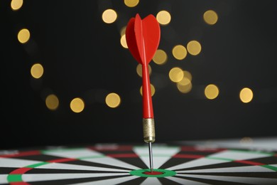 Photo of Red arrow hitting target on dart board against black background with blurred lights, closeup