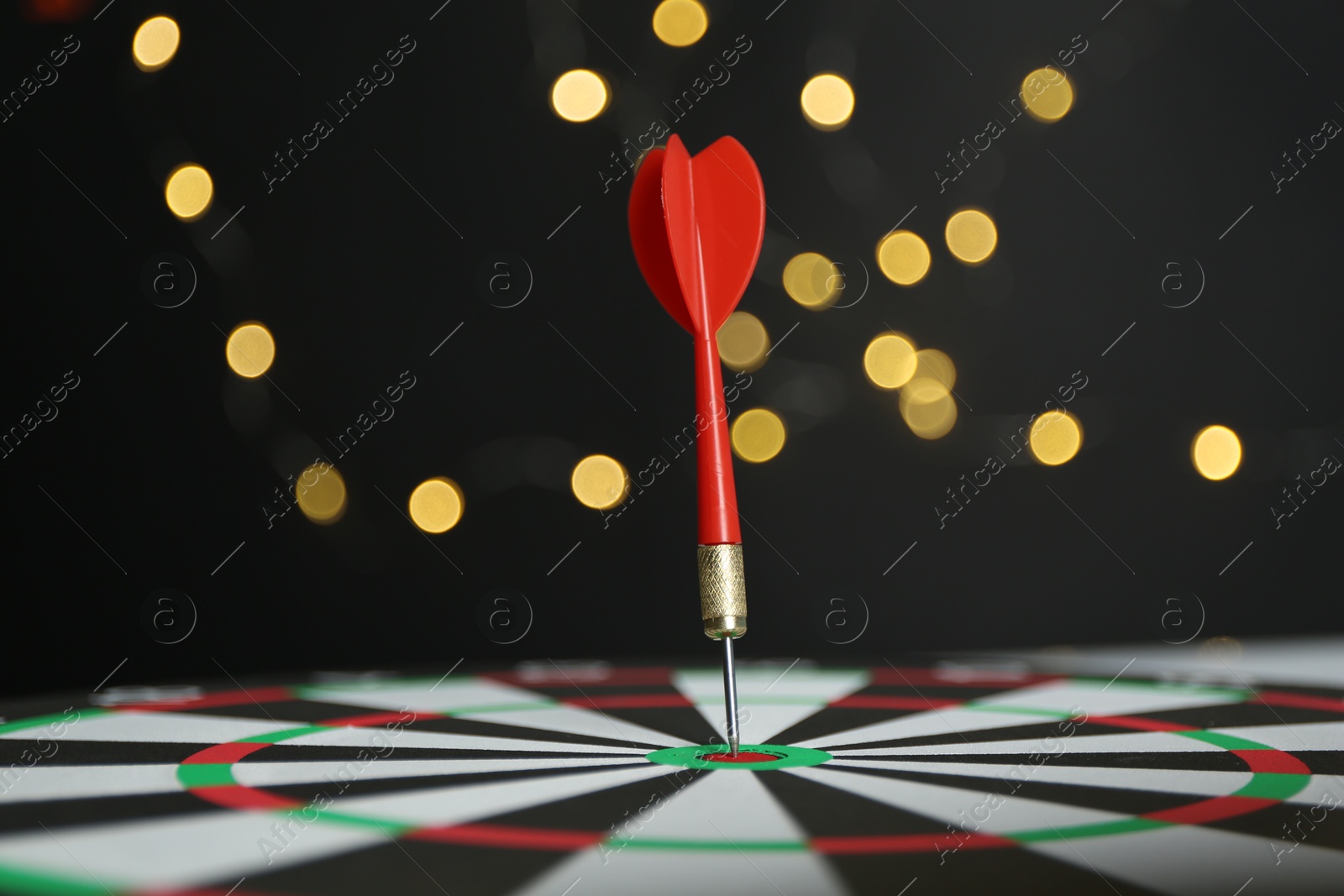 Photo of Red arrow hitting target on dart board against black background with blurred lights, closeup