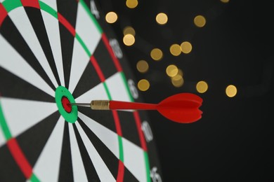 Photo of Red arrow hitting target on dart board against black background with blurred lights, closeup