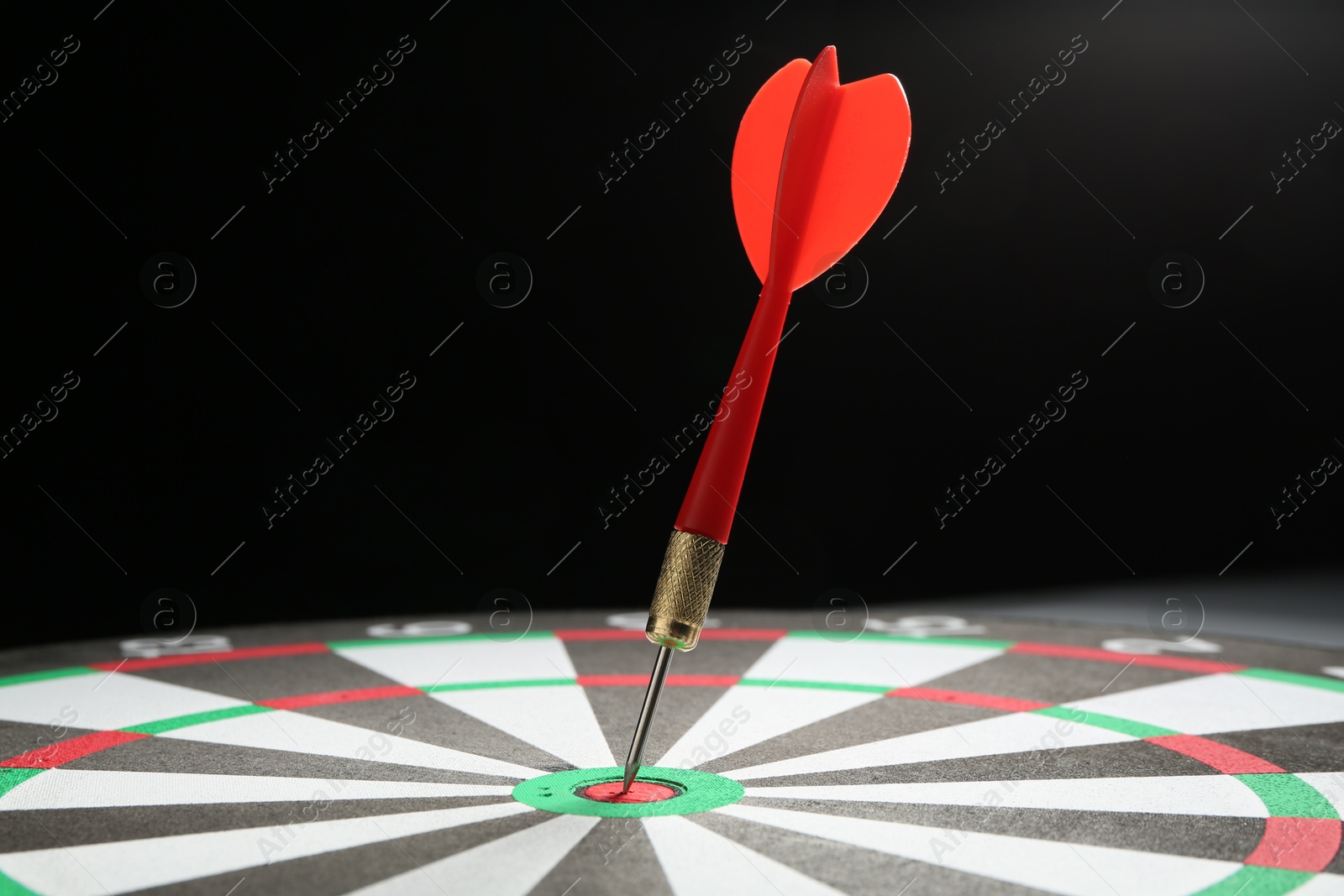 Photo of Red arrow hitting target on dart board against black background, closeup