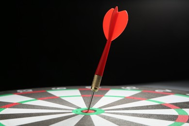 Photo of Red arrow hitting target on dart board against black background, closeup