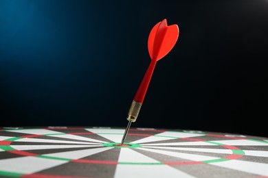 Photo of Red arrow hitting target on dart board against blue background, closeup