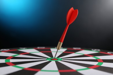 Photo of Red arrow hitting target on dart board against blue background, closeup