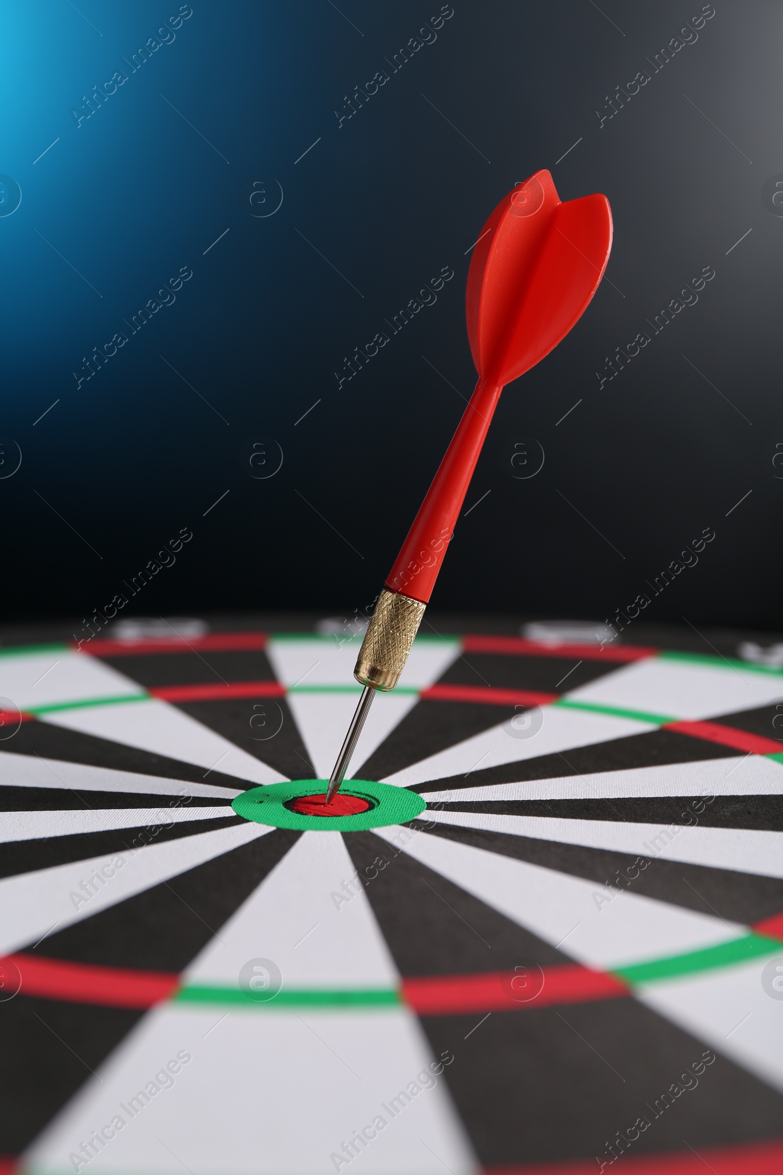 Photo of Red arrow hitting target on dart board against blue background, closeup