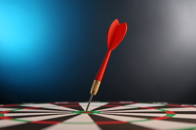 Photo of Red arrow hitting target on dart board against blue background, closeup