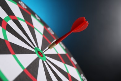 Photo of Red arrow hitting target on dart board against blue background, closeup