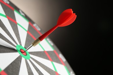 Photo of Red arrow hitting target on dart board against black background, closeup