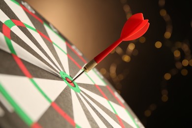 Photo of Red arrow hitting target on dart board against black background with blurred lights, closeup