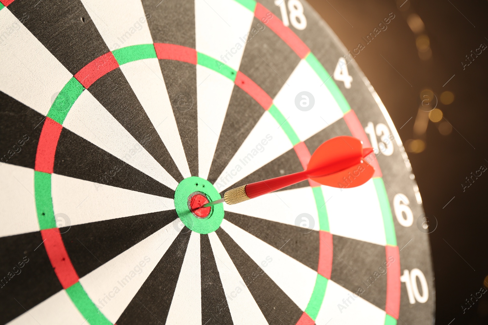 Photo of Red arrow hitting target on dart board against black background with blurred lights, closeup