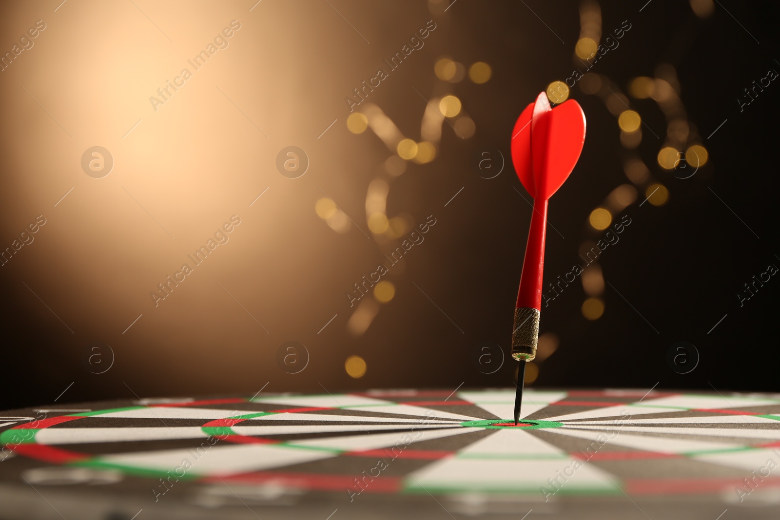 Photo of Red arrow hitting target on dart board against black background with blurred lights, closeup. Space for text