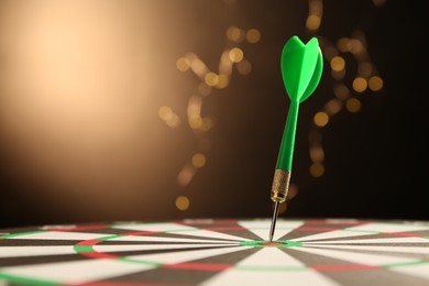 Photo of Green arrow hitting target on dart board against black background with blurred lights, closeup. Space for text