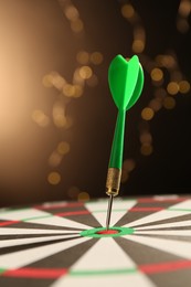 Photo of Green arrow hitting target on dart board against black background with blurred lights, closeup