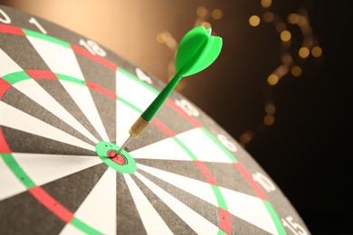 Photo of Green arrow hitting target on dart board against black background with blurred lights, closeup