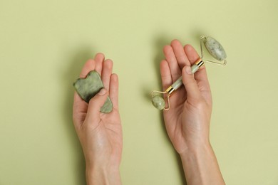 Photo of Woman with face roller and gua sha tool on light green background, top view