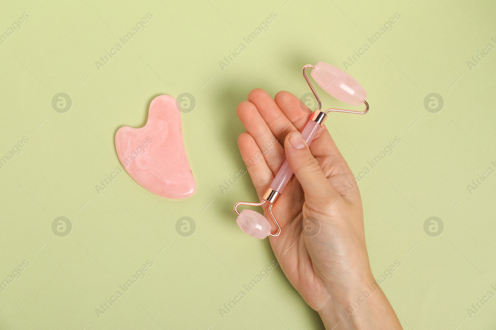 Photo of Woman with face roller and gua sha tool on light green background, top view