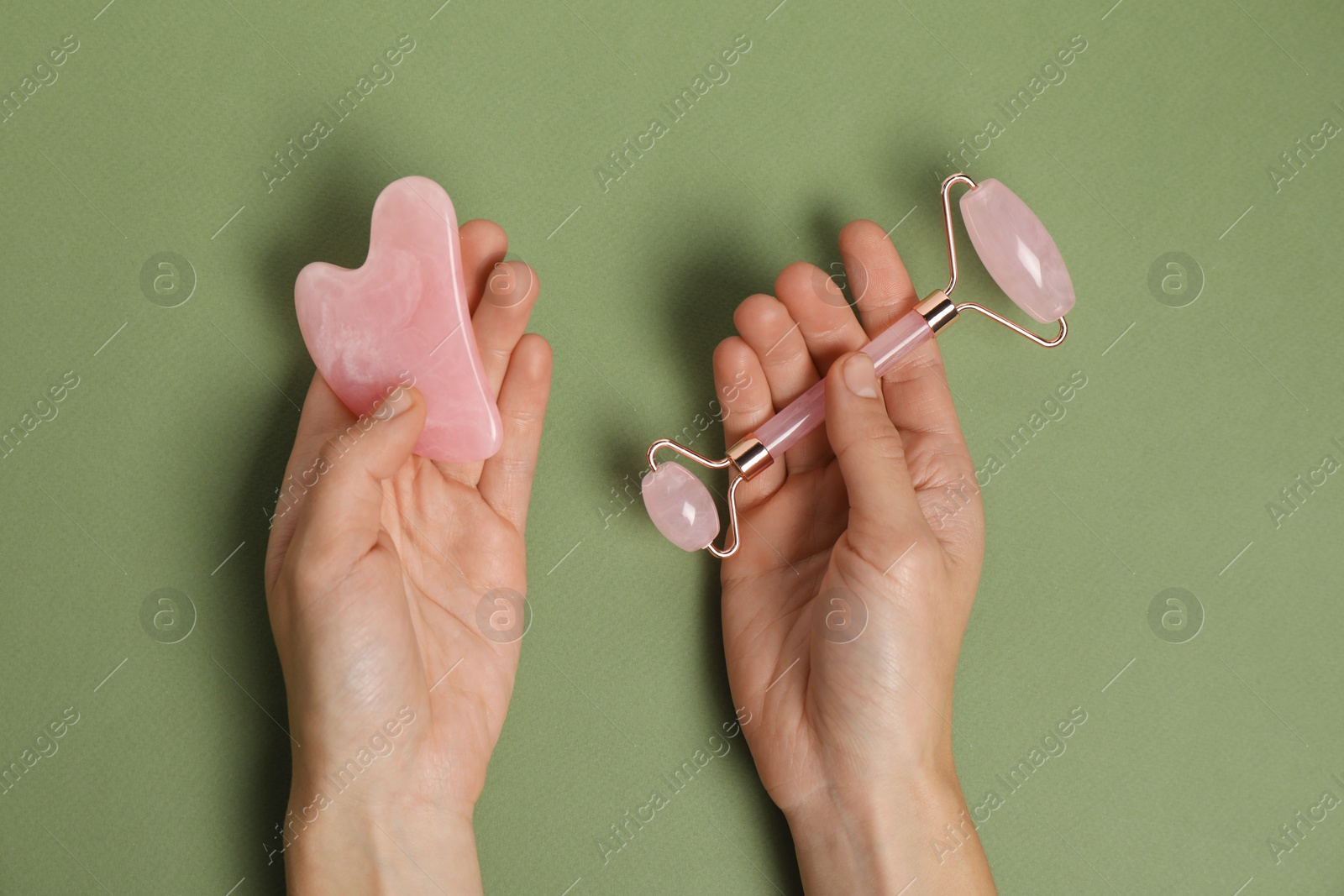 Photo of Woman with face roller and gua sha tool on green background, top view