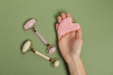 Photo of Woman with face rollers and gua sha tool on green background, top view