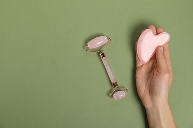 Photo of Woman with face roller and gua sha tool on green background, top view. Space for text