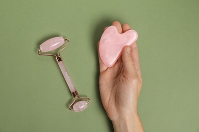 Photo of Woman with face roller and gua sha tool on green background, top view