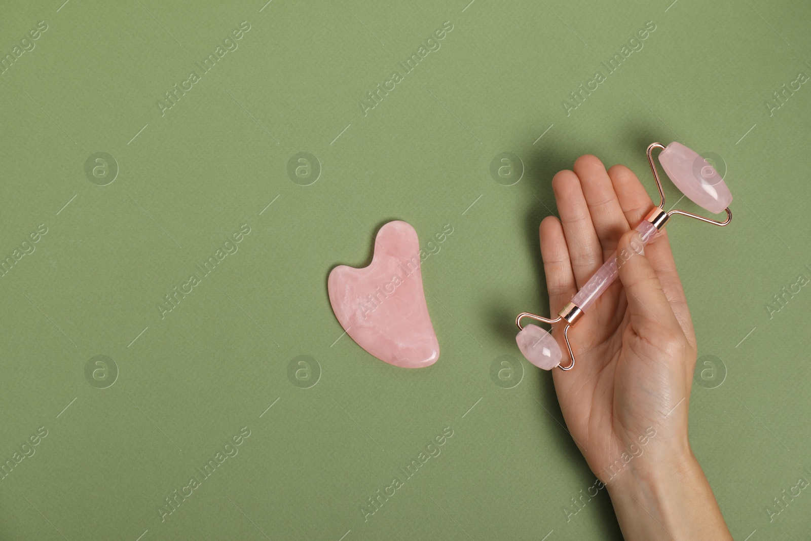 Photo of Woman with face roller and gua sha tool on green background, top view. Space for text