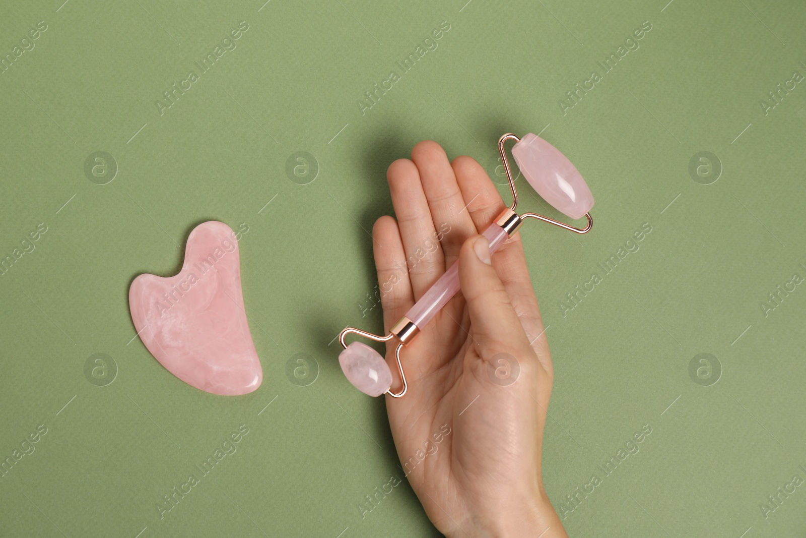 Photo of Woman with face roller and gua sha tool on green background, top view