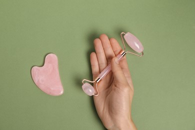 Photo of Woman with face roller and gua sha tool on green background, top view