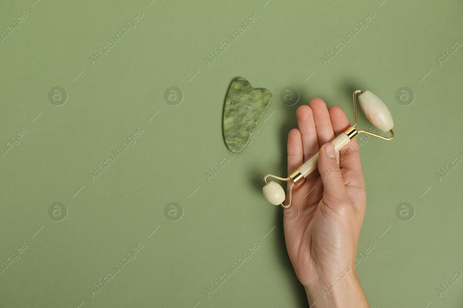 Photo of Woman with face roller and gua sha tool on green background, top view. Space for text