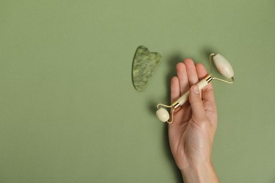 Photo of Woman with face roller and gua sha tool on green background, top view. Space for text