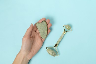 Photo of Woman with gua sha tool and face roller on light blue background, top view