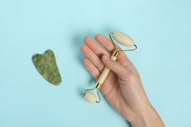 Photo of Woman with face roller and gua sha tool on light blue background, top view