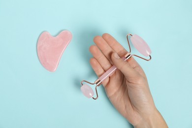 Photo of Woman with face roller and gua sha tool on light blue background, top view