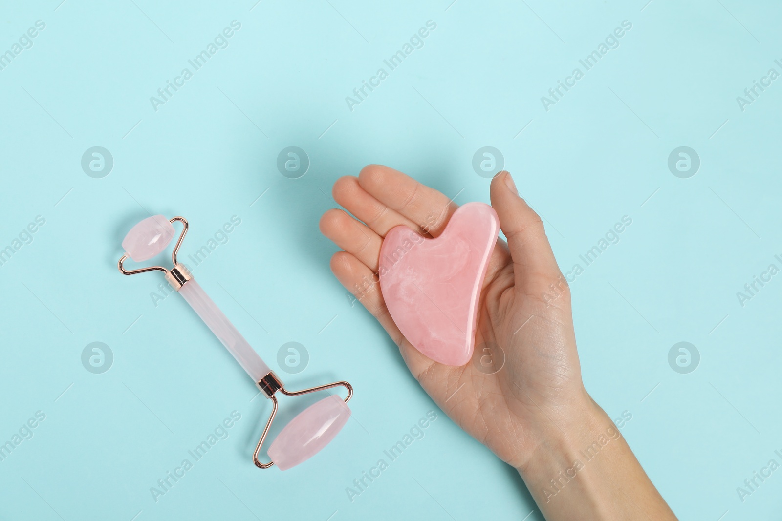 Photo of Woman with face roller and gua sha tool on light blue background, top view