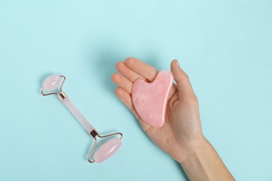 Photo of Woman with face roller and gua sha tool on light blue background, top view