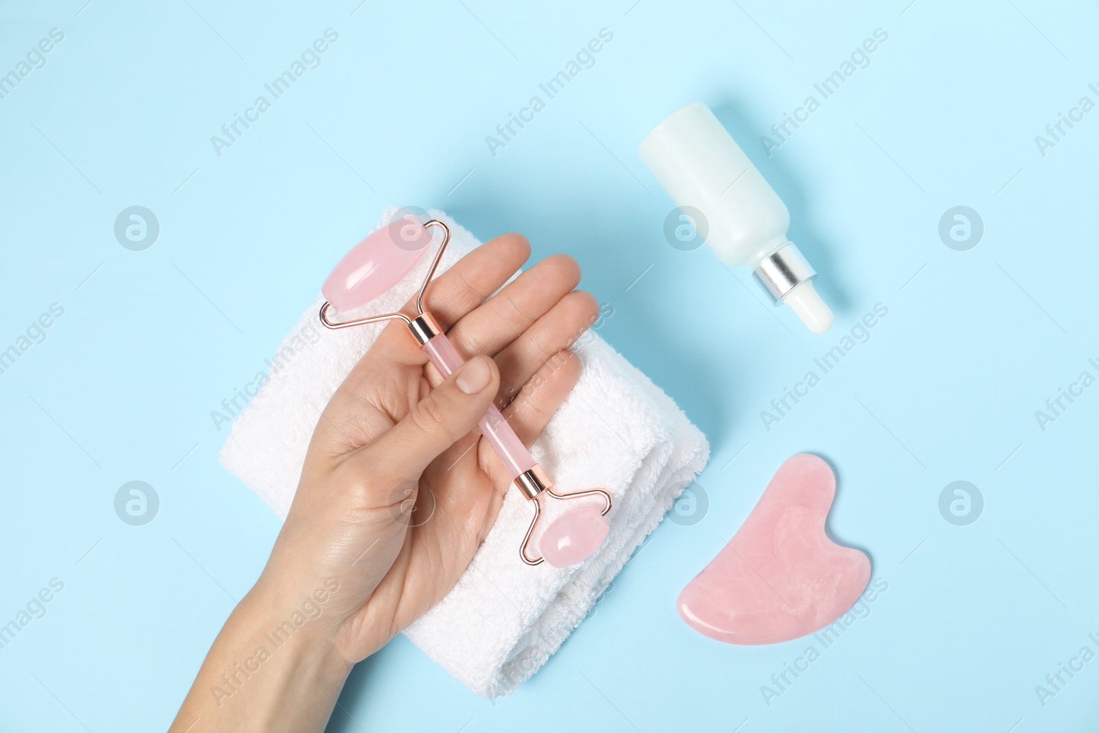 Photo of Woman with face roller, gua sha tool, cosmetic product and towel on light blue background, top view