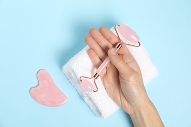 Photo of Woman with face roller, gua sha tool and towel on light blue background, top view