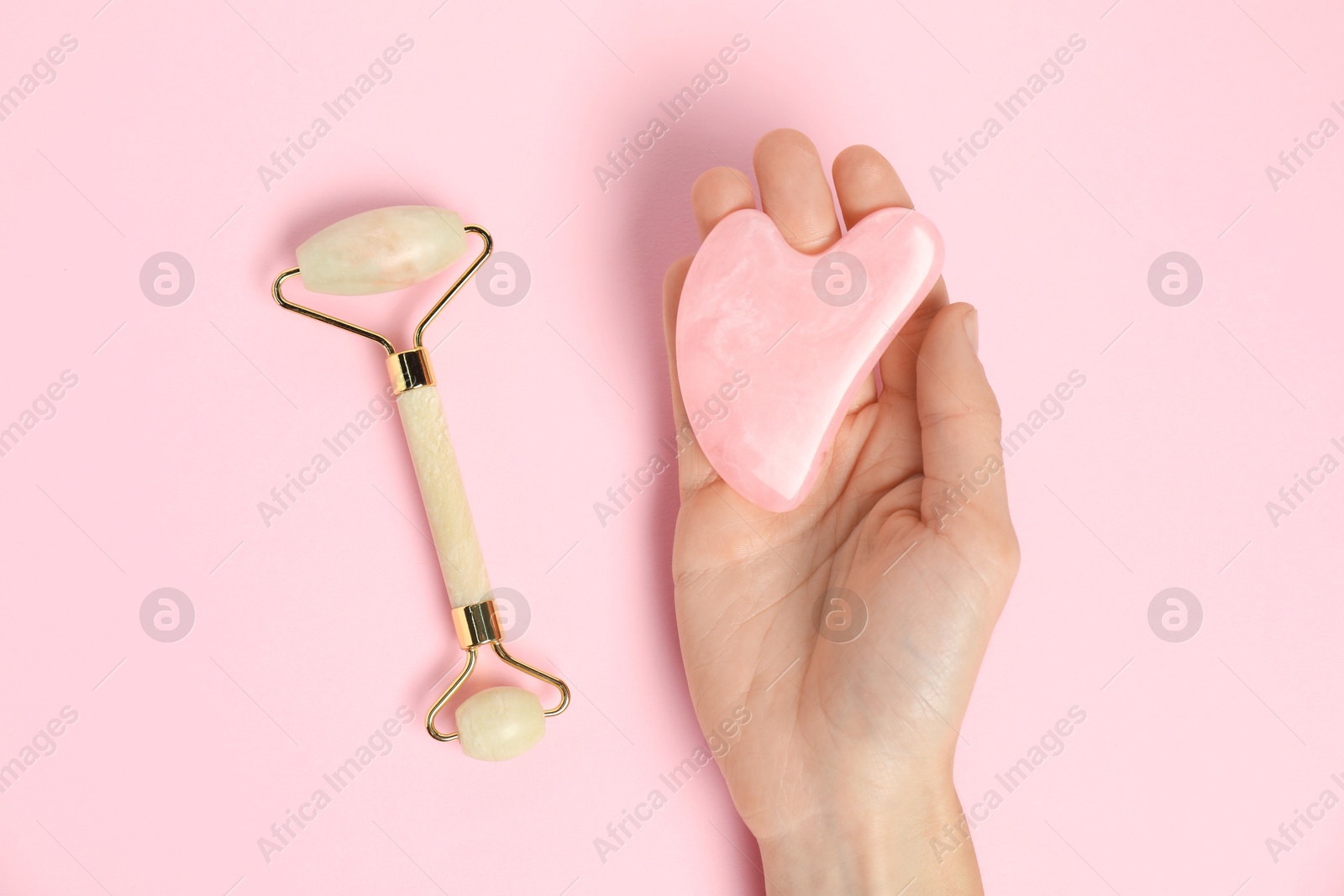 Photo of Woman with gua sha tool and face roller on pink background, top view