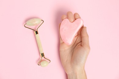 Photo of Woman with gua sha tool and face roller on pink background, top view