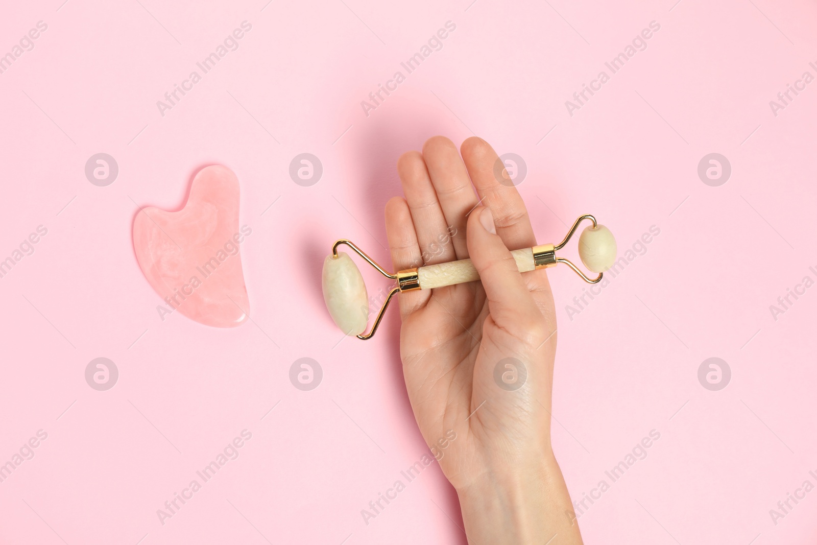 Photo of Woman with face roller and gua sha tool on pink background, top view